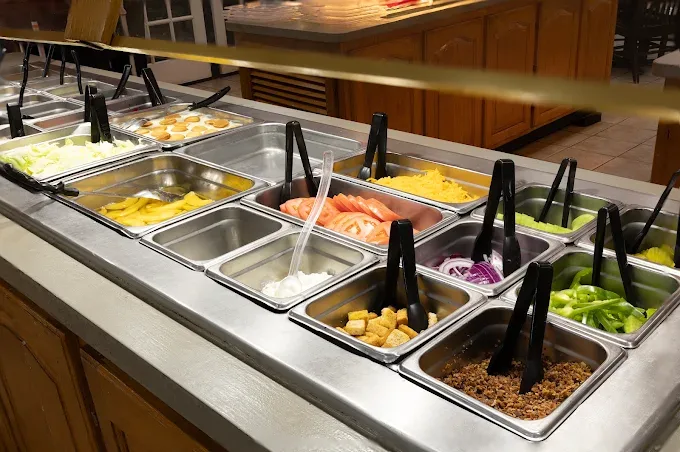 Salad bar counter with fresh vegetables, shredded cheese, and sliced tomatoes