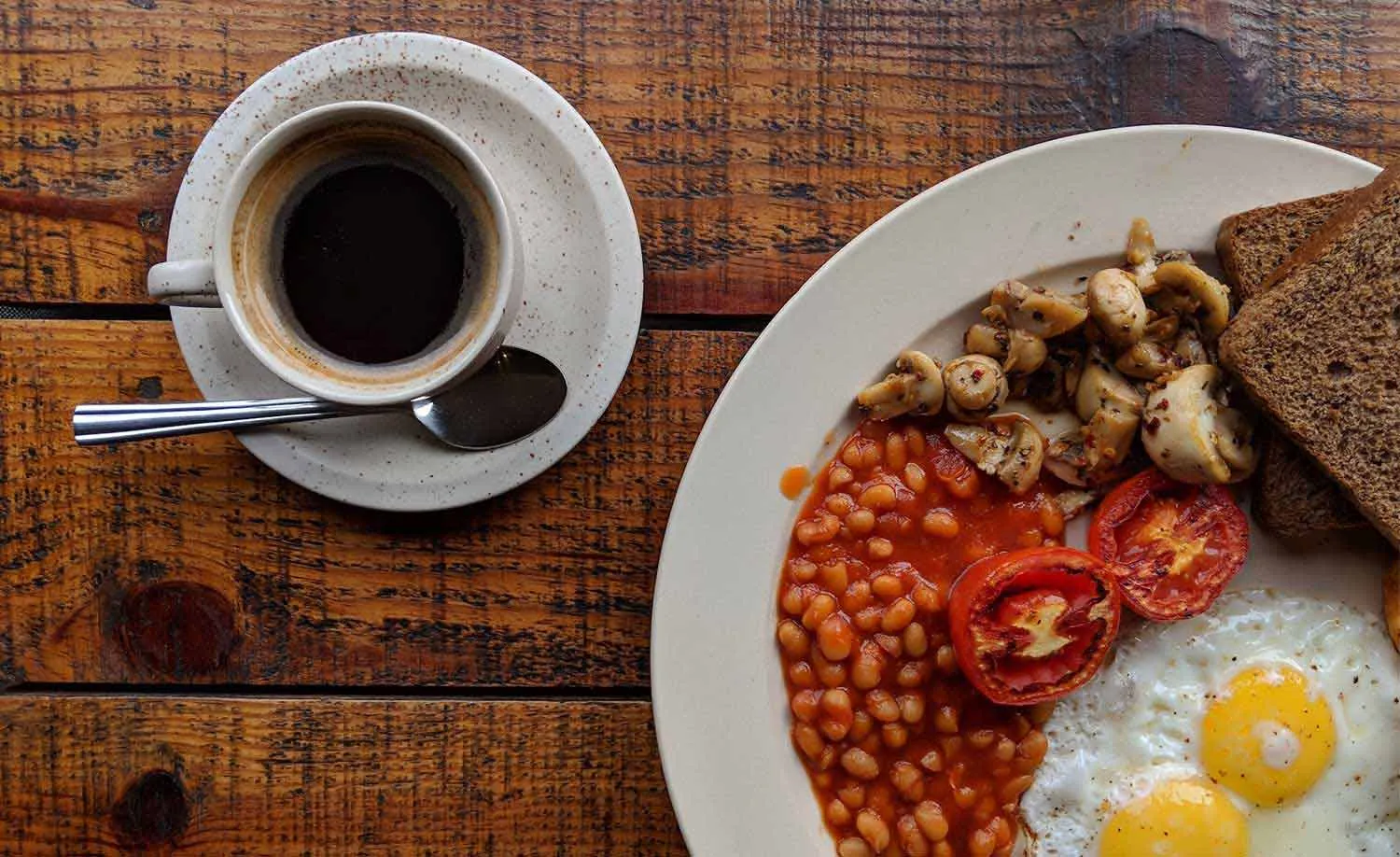 A hearty breakfast plate — eggs, baked beans, tomato and toast — with fresh coffee at Carolina Fine Foods